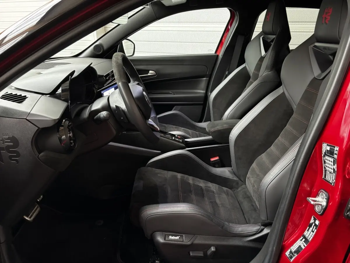Vue intérieure côté conducteur de l'Alfa Romeo Junior rouge 2024 avec sièges sport Sabelt noirs et volant cuir multifonctions.