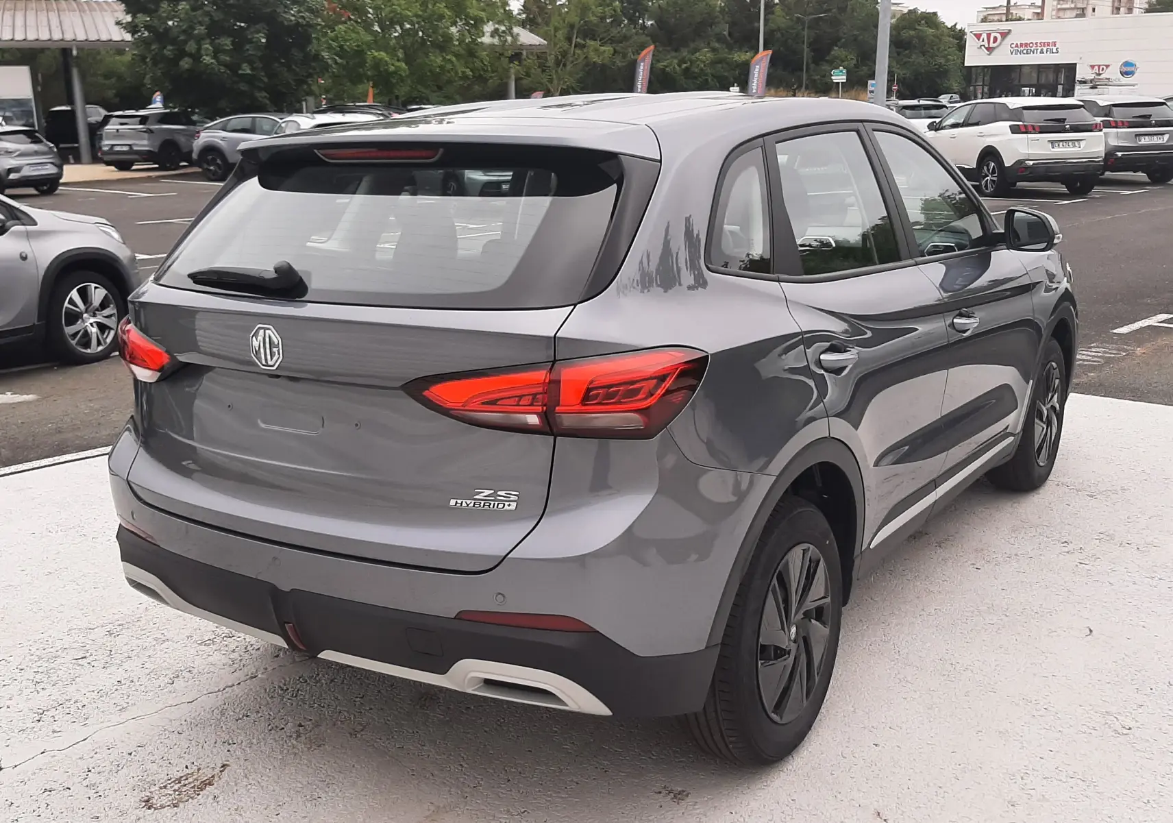 Vue 3/4 arrière droite du MG Motor ZS 1.5 Hybrid+ 197ch 2026 en Camden Grey avec feux arrière LED distinctifs.