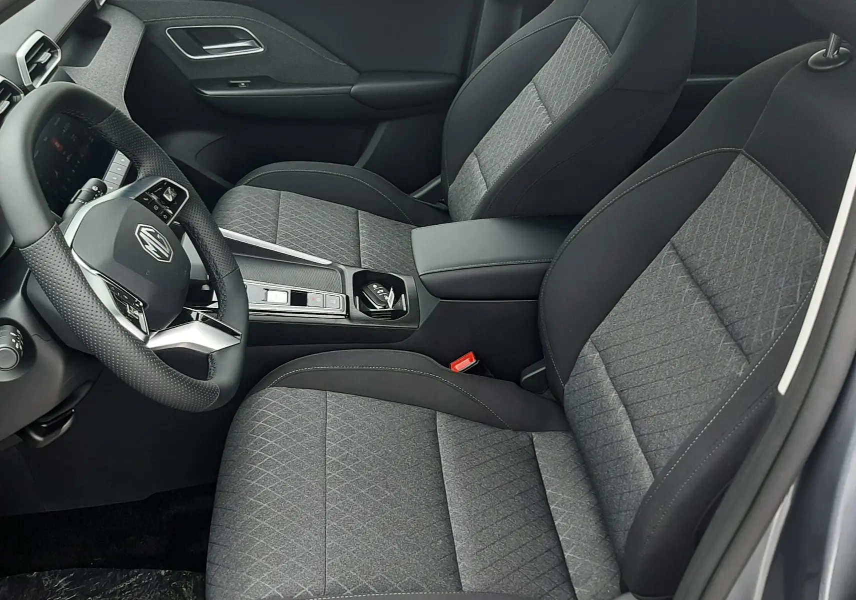 Vue intérieure côté conducteur du MG Motor ZS 1.5 Hybrid+ 197ch 2026, sièges tissu gris Camden Grey avec console centrale moderne.