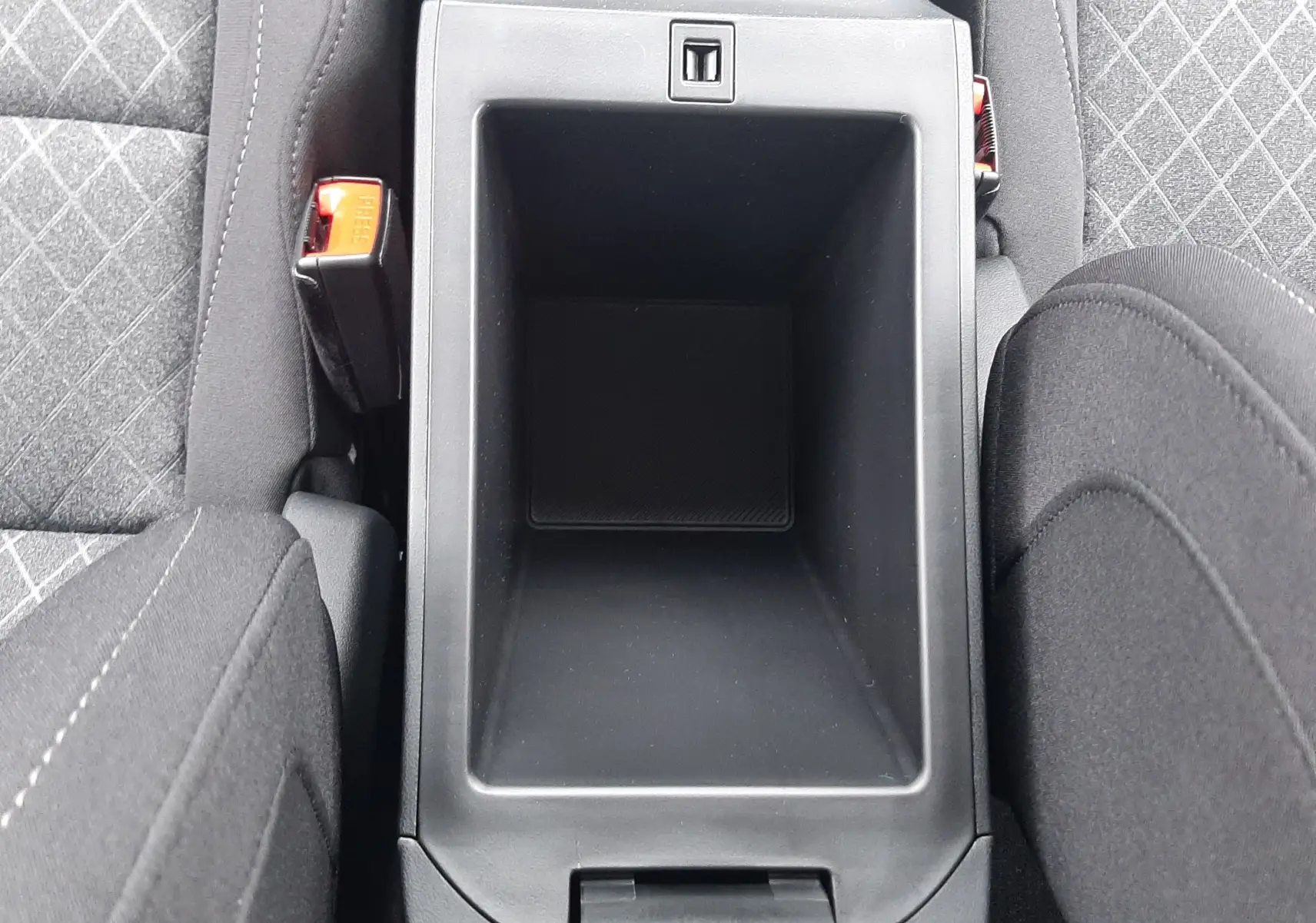 Vue plongeante sur le rangement central noir entre les sièges tissu gris à motifs du MG Motor ZS 1.5 Hybrid+ 2026.