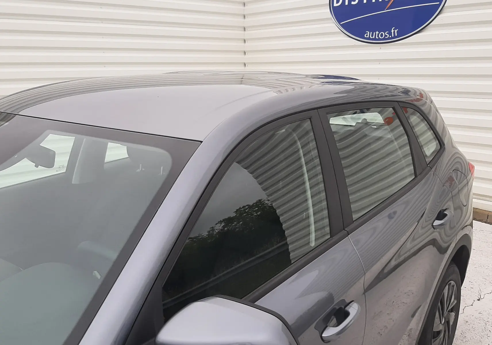 Vue 3/4 avant droit du MG MOTOR ZS 1.5 HYBRID+ 197CH 2026 en gris Camden, avec rétroviseur et vitres teintées visibles.