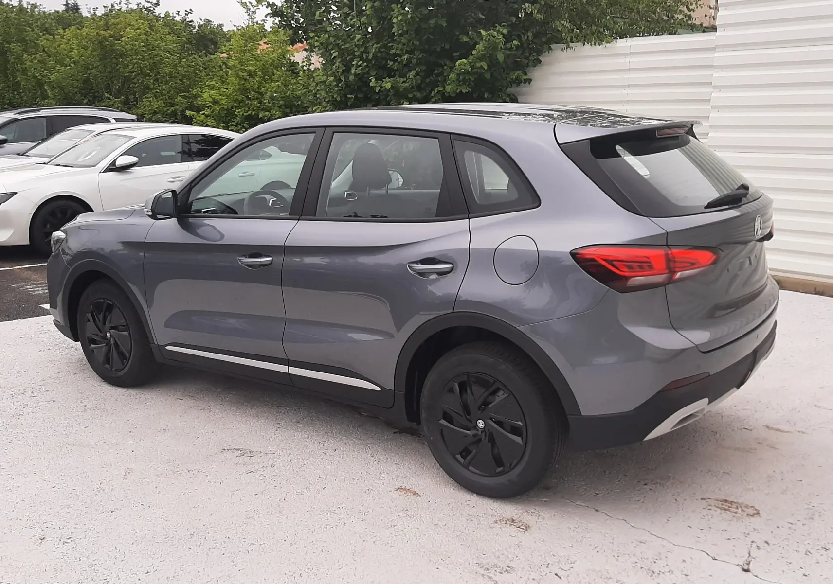 Vue 3/4 arrière droite du MG ZS 1.5 HYBRID+ 197CH 2026 en gris Camden avec jantes noires et feux arrière allumés.