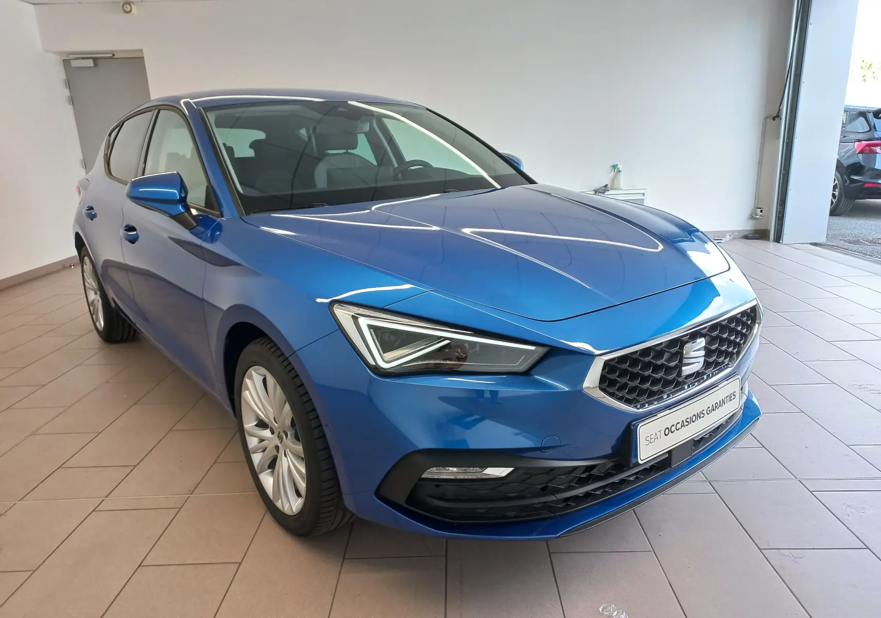 SEAT Leon 1.5 eTSI 115 DSG7 Copa bleu saphir en 3/4 avant droit, intérieur showroom lumineux.