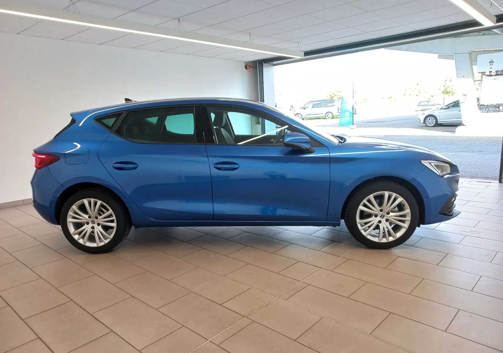 Profil côté gauche d'une SEAT LEON 1.5 eTSI 115 DSG7 COPA en bleu saphir, avec vitres arrière surteintées en intérieur showroom.
