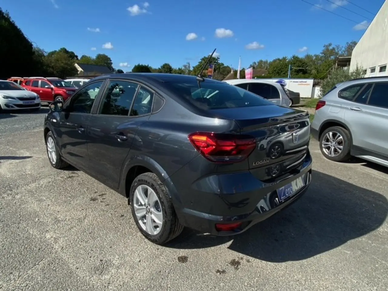 Vue 3/4 arrière droite d'une Dacia Logan gris métallisé 2022 avec feux arrière LED et caméra de recul visible.