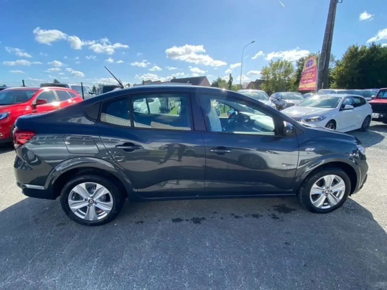 Profil côté gauche d'une berline Dacia Logan gris métallisé 2022 garée en extérieur sous un ciel bleu.