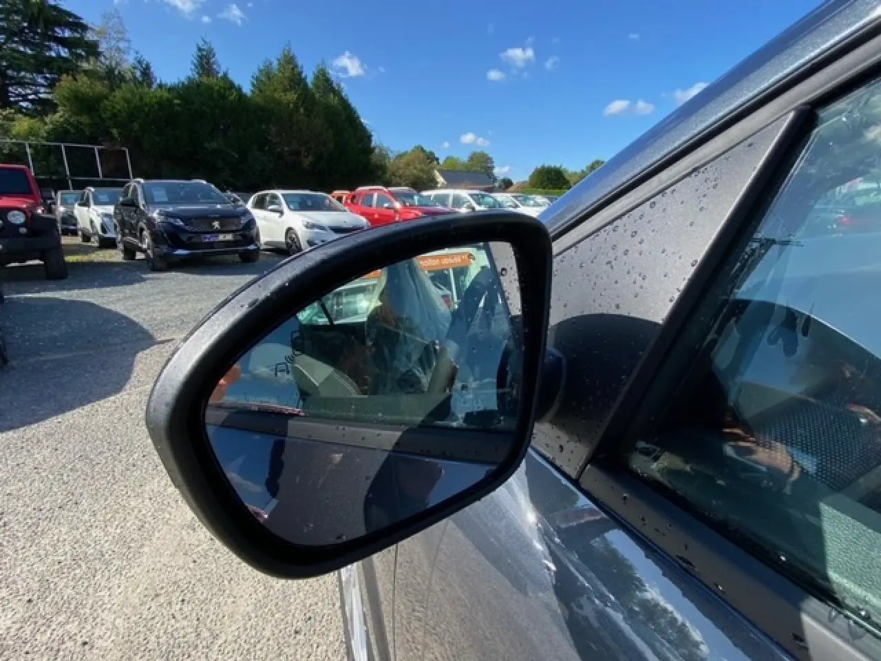 Rétroviseur côté gauche d'une Dacia Logan gris 2022 avec gouttes d'eau sur la carrosserie, vue rapprochée extérieure.