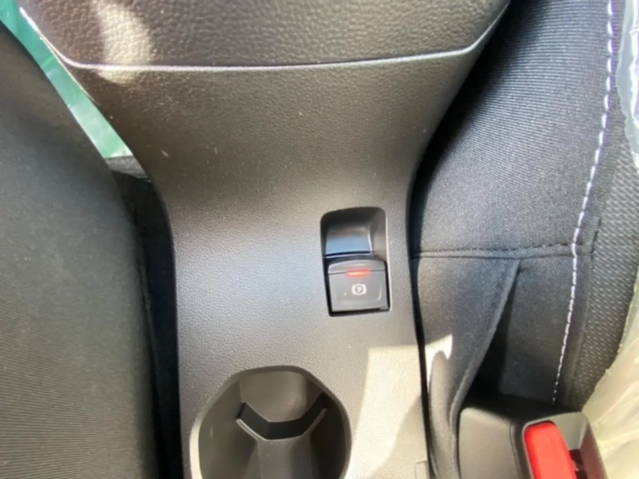 Gros plan sur le frein à main électronique et porte-gobelet entre les sièges avant d'une Dacia Logan gris 2022.