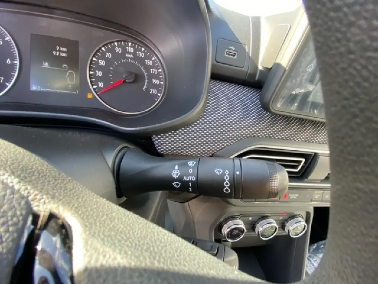 Gros plan sur la manette d'essuie-glace et le tableau de bord gris d'une Dacia Logan 2022 avec compteur et commandes visibles.