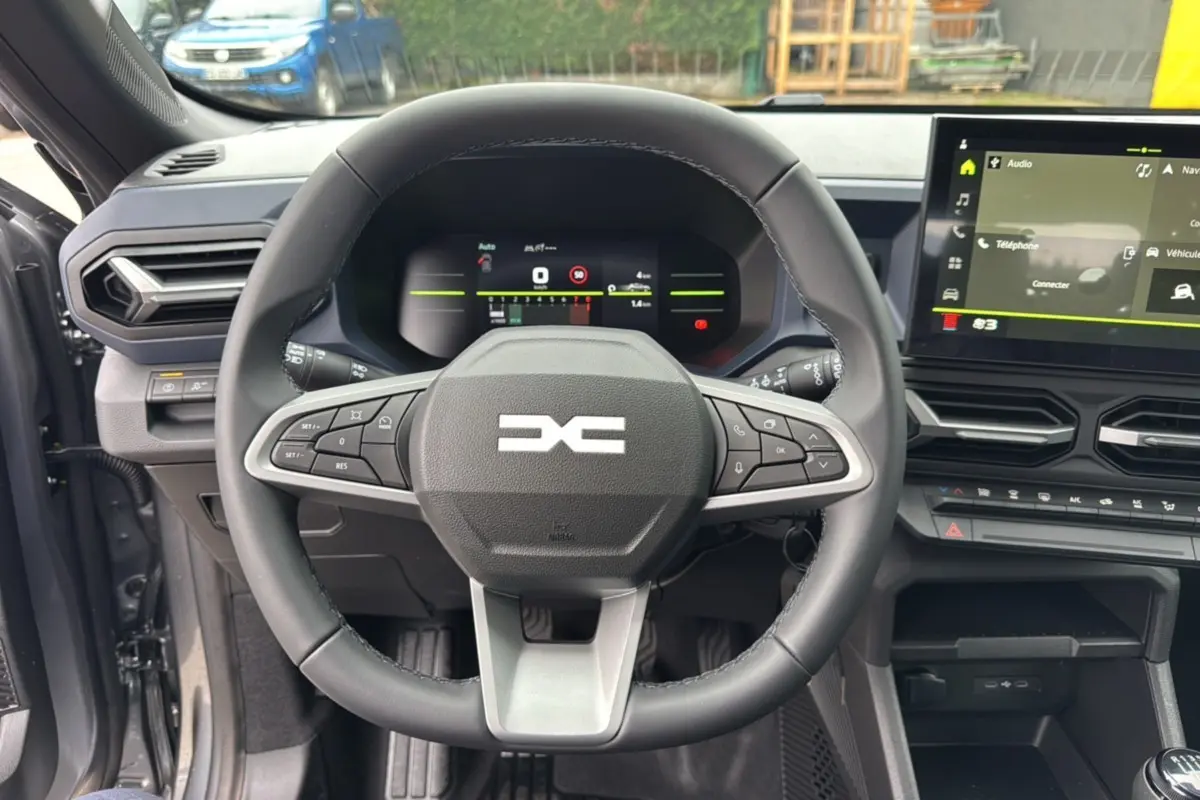 Vue intérieure centrée sur le volant du Dacia Duster 2025 gris schiste, avec tableau de bord numérique et écran tactile.