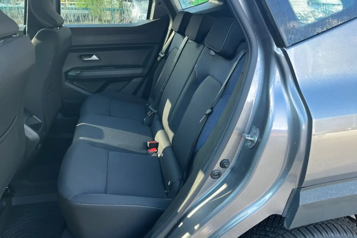 Vue côté droit sur l'intérieur arrière du Dacia Duster 2025 gris schiste, montrant les sièges arrière en tissu noir.