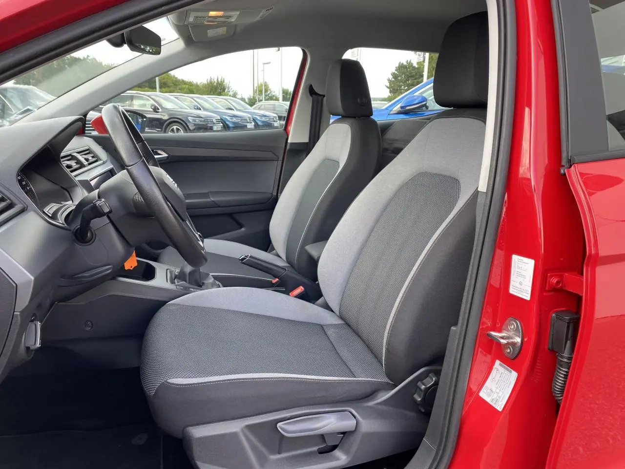 Vue intérieure côté conducteur de la SEAT IBIZA rouge pur 2021, avec sièges tissu gris et volant cuir multifonctions.