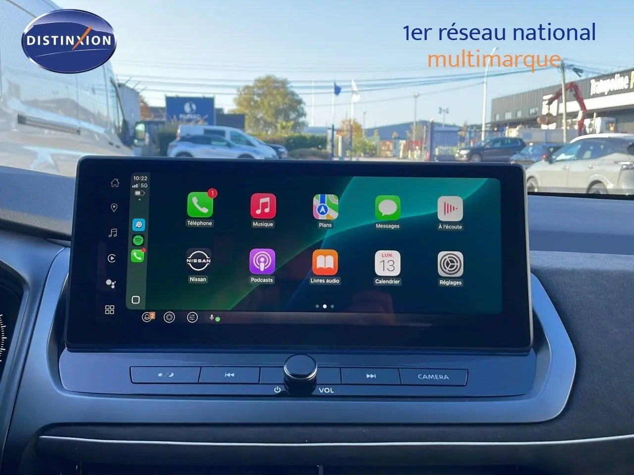 Écran tactile central du Nissan Qashqai 2025 affichant les applications Apple CarPlay, avec vue extérieure floutée.