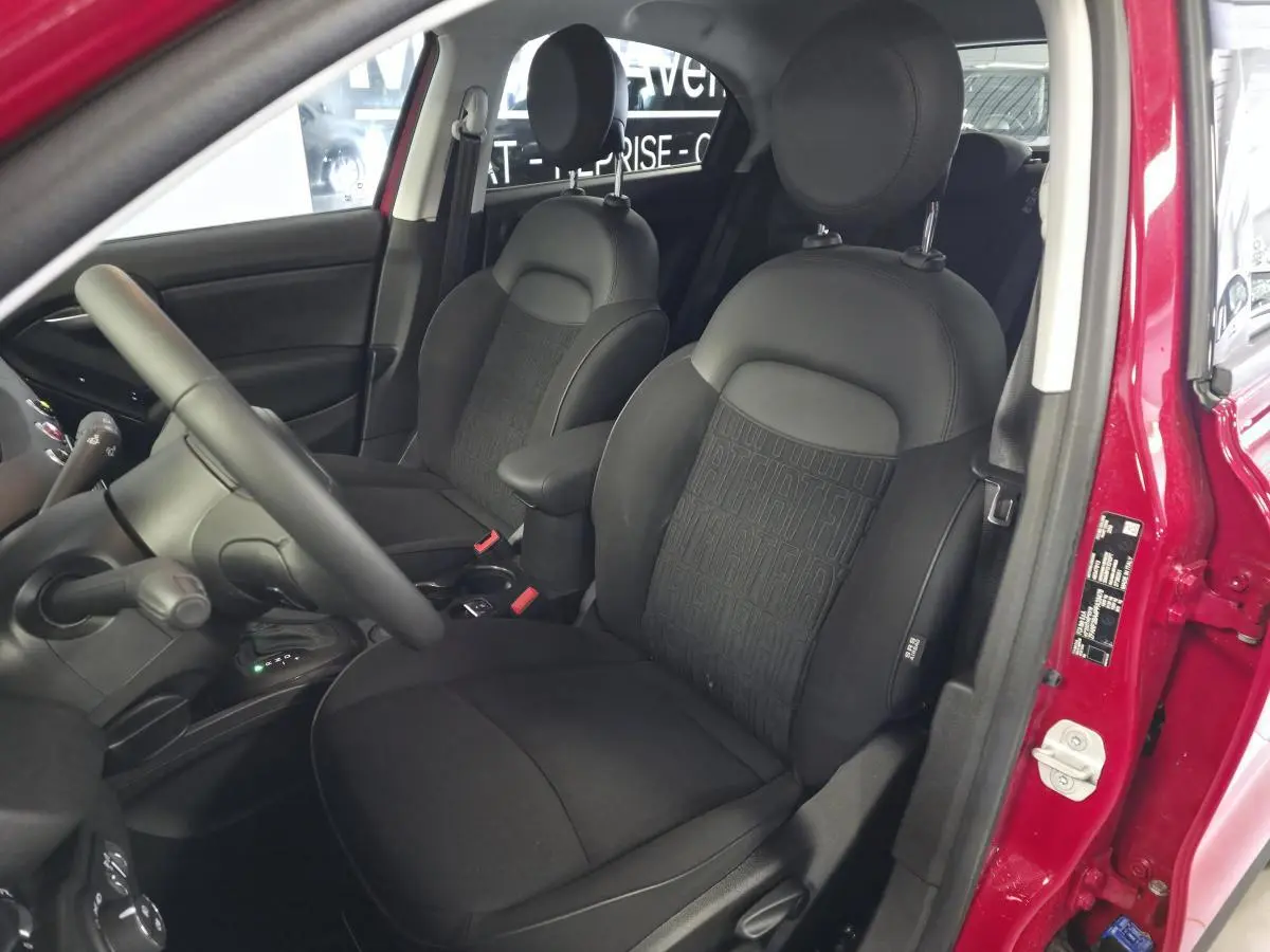 Vue intérieure côté conducteur du Fiat 500X rouge 2024, sièges tissu noir avec monogramme FIAT et accoudoir central.