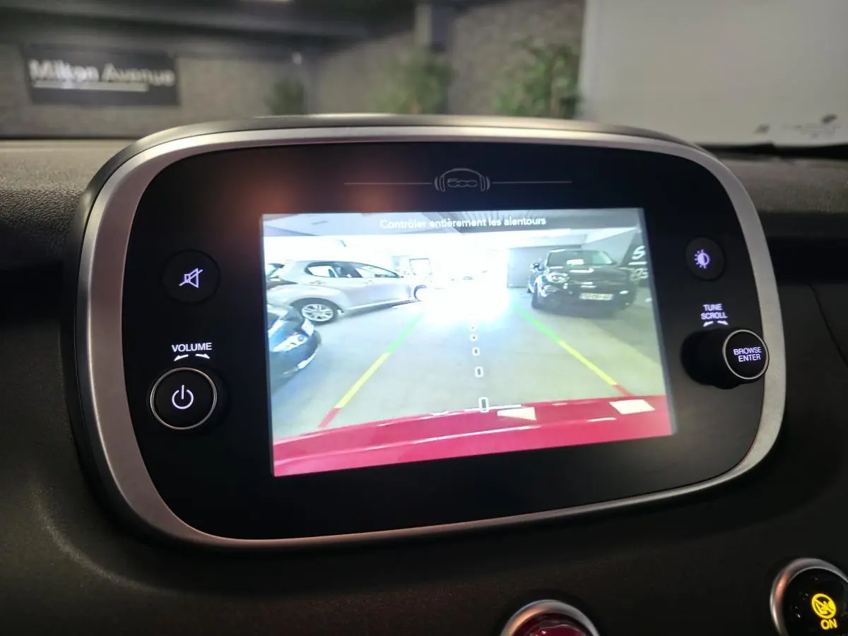 Écran multimédia de la Fiat 500X rouge montrant la caméra de recul avec vue arrière en parking intérieur.