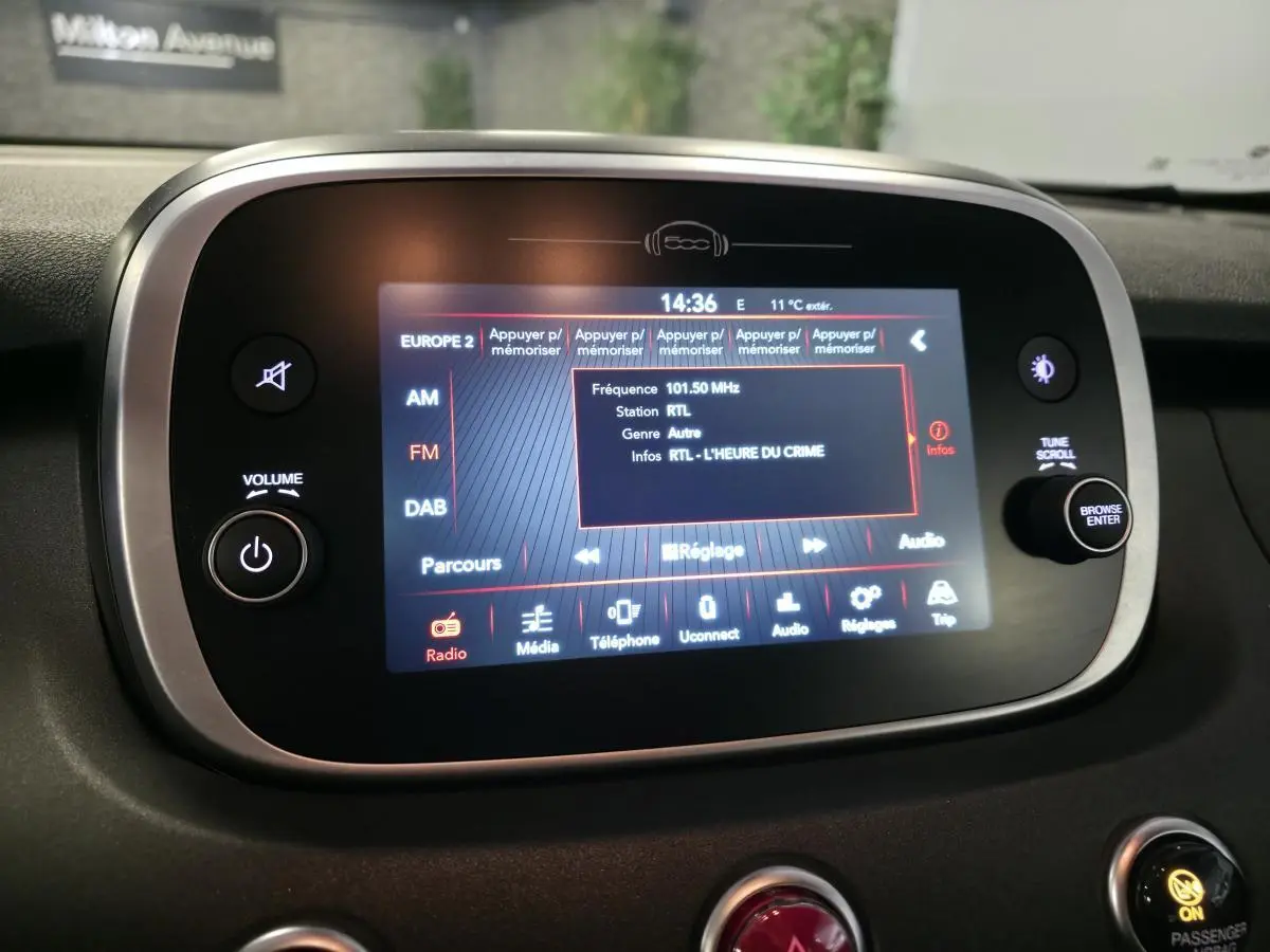 Écran tactile multimédia de la Fiat 500X rouge 2024 affichant la radio RTL avec commandes autour en tableau de bord noir.