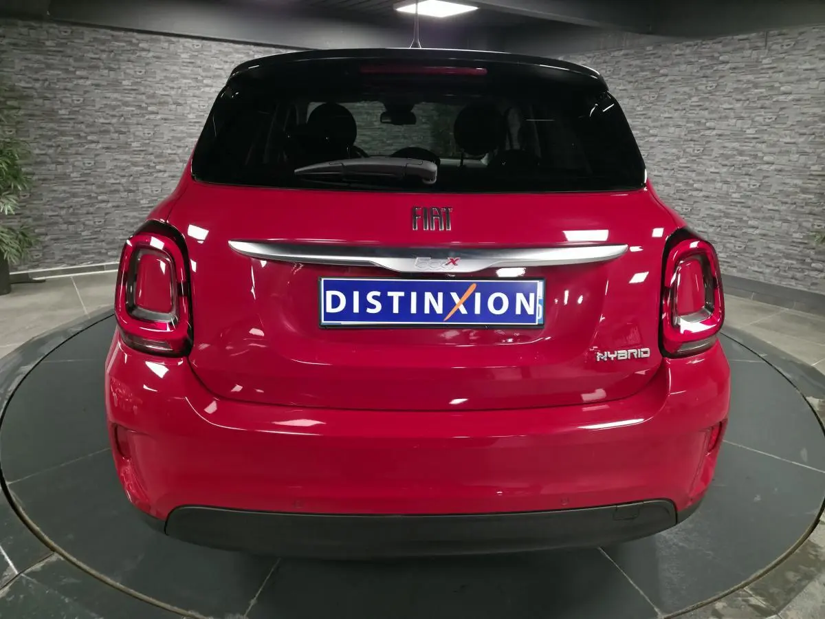 Vue arrière d'un Fiat 500X rouge Passion avec logo FIAT et badge Hybrid sur fond intérieur gris.