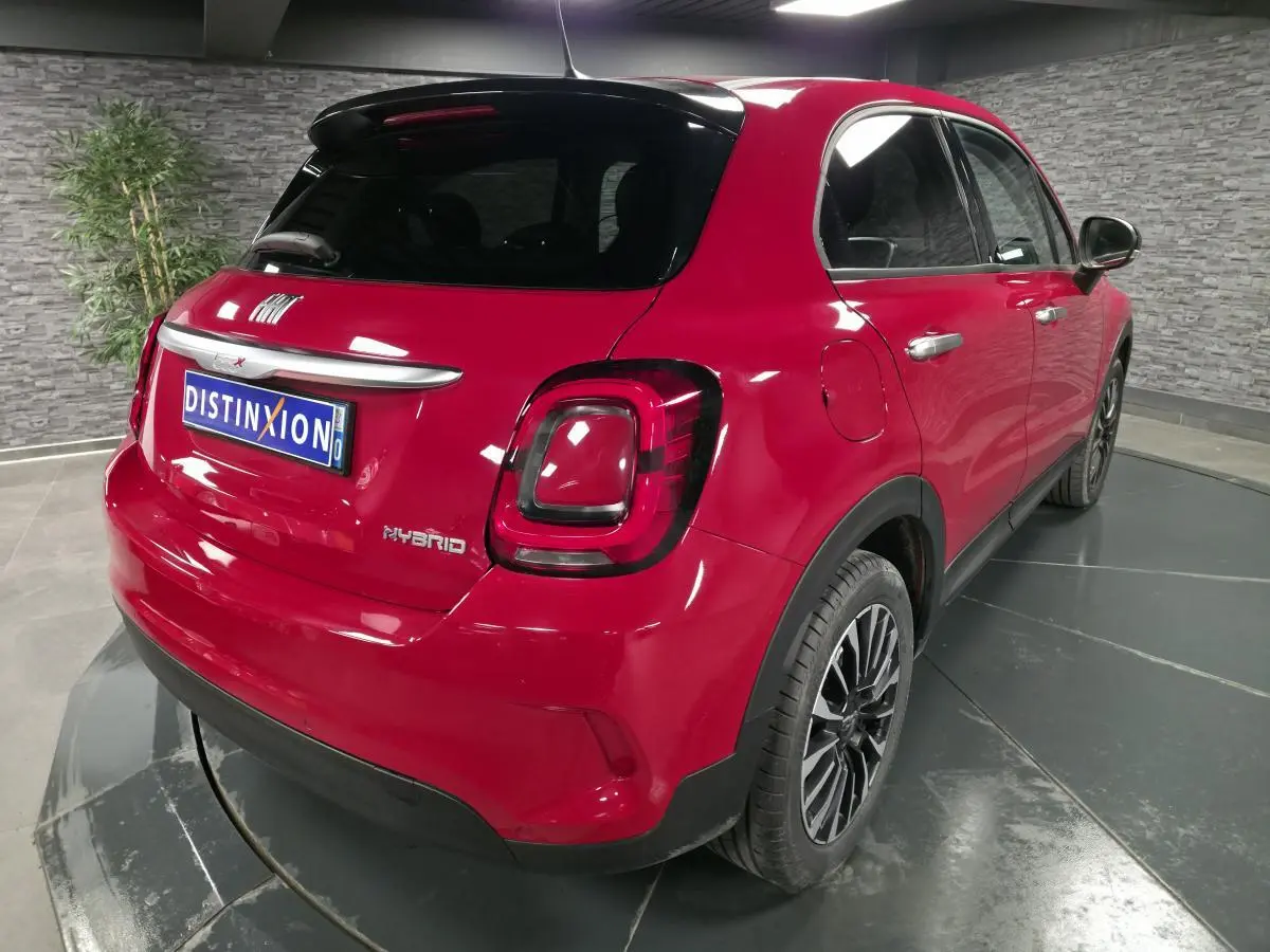Fiat 500X rouge vue 3/4 arrière droit, avec toit noir et jantes alliage 17 pouces dans un showroom.
