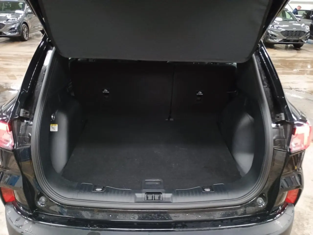 Coffre ouvert d'un Ford Kuga noir Obsidien, vue arrière montrant l'espace de chargement vide et les feux arrière allumés.