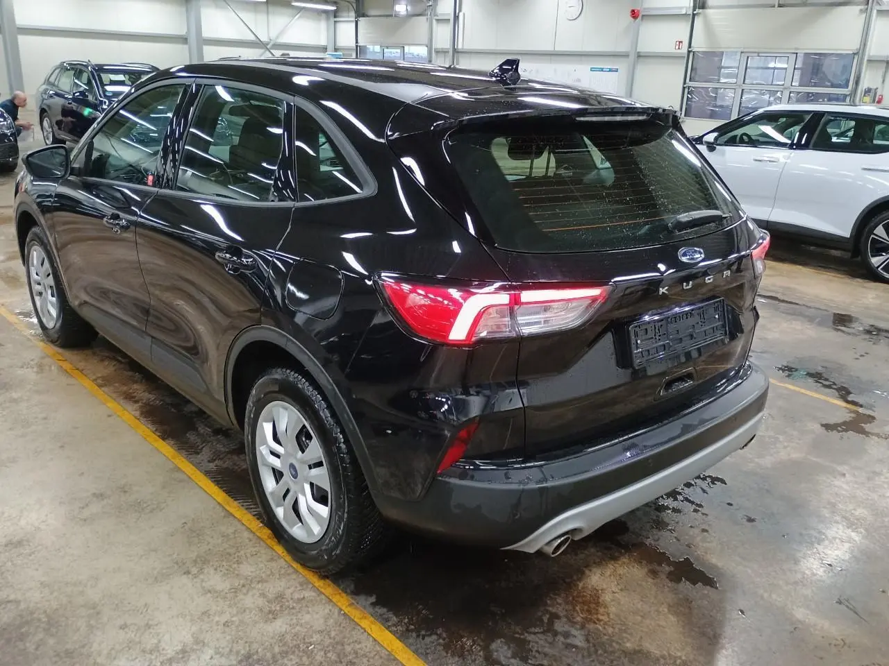 Vue 3/4 arrière droite d'un Ford Kuga noir Obsidien 2024 dans un garage, avec feux arrière allumés.