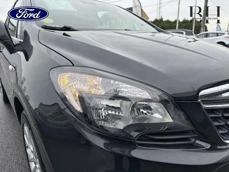Gros plan sur le phare avant gauche d’un Opel Mokka noir carbone, avec calandre chromée visible.