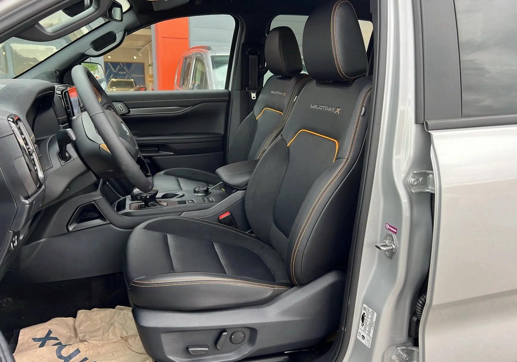 Vue intérieure côté conducteur du Ford Ranger 2026 gris iconic, sièges Wildtrak X avec surpiqûres orange et volant cuir multifonctions.