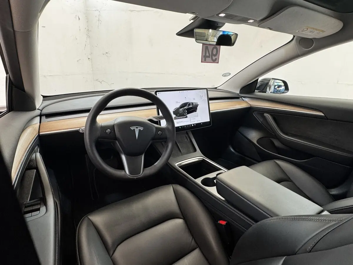 Intérieur Tesla Model 3 noir vue côté conducteur, tableau de bord épuré avec grand écran tactile central.