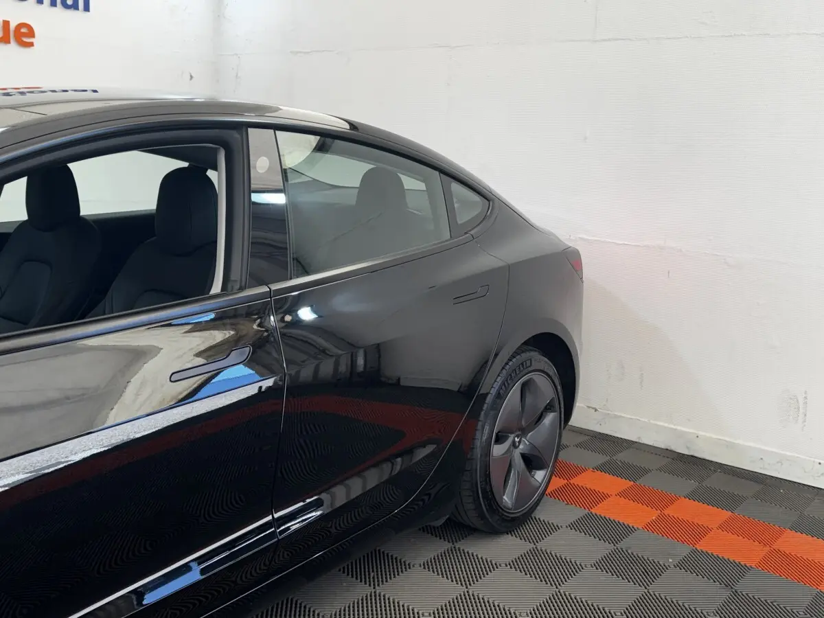 Vue côté gauche arrière d'une Tesla Model 3 Grande Autonomie noire, avec jante aérodynamique et poignée affleurante.