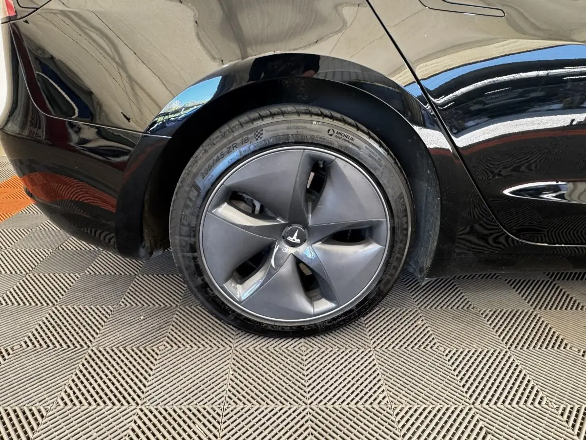 Gros plan sur la roue arrière droite noire d'une Tesla Model 3 Grande Autonomie 2023 avec jante aérodynamique.