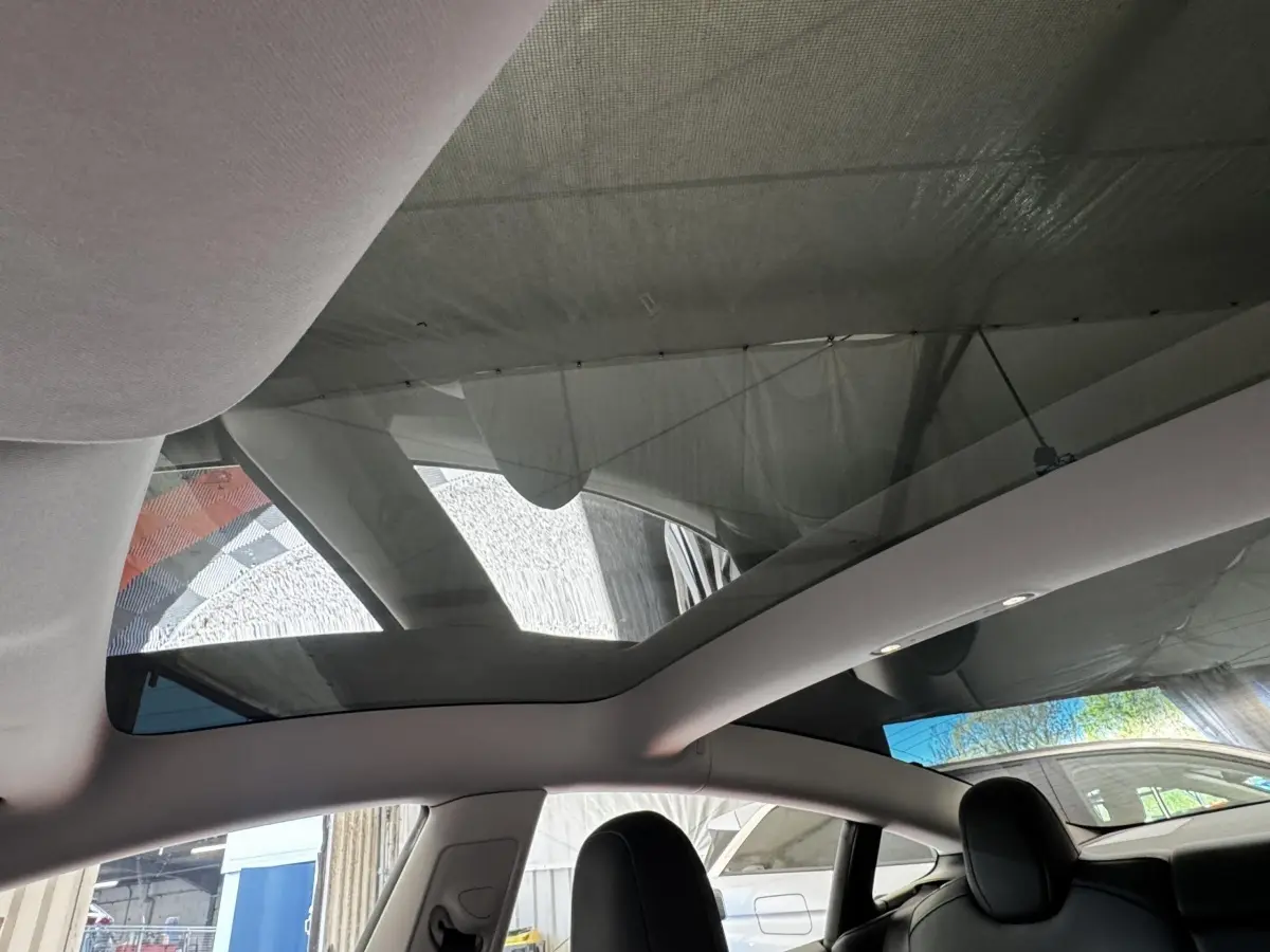Vue intérieure du toit panoramique en verre d'une Tesla Model 3 noire 2023, avec sièges avant en cuir noir visibles.