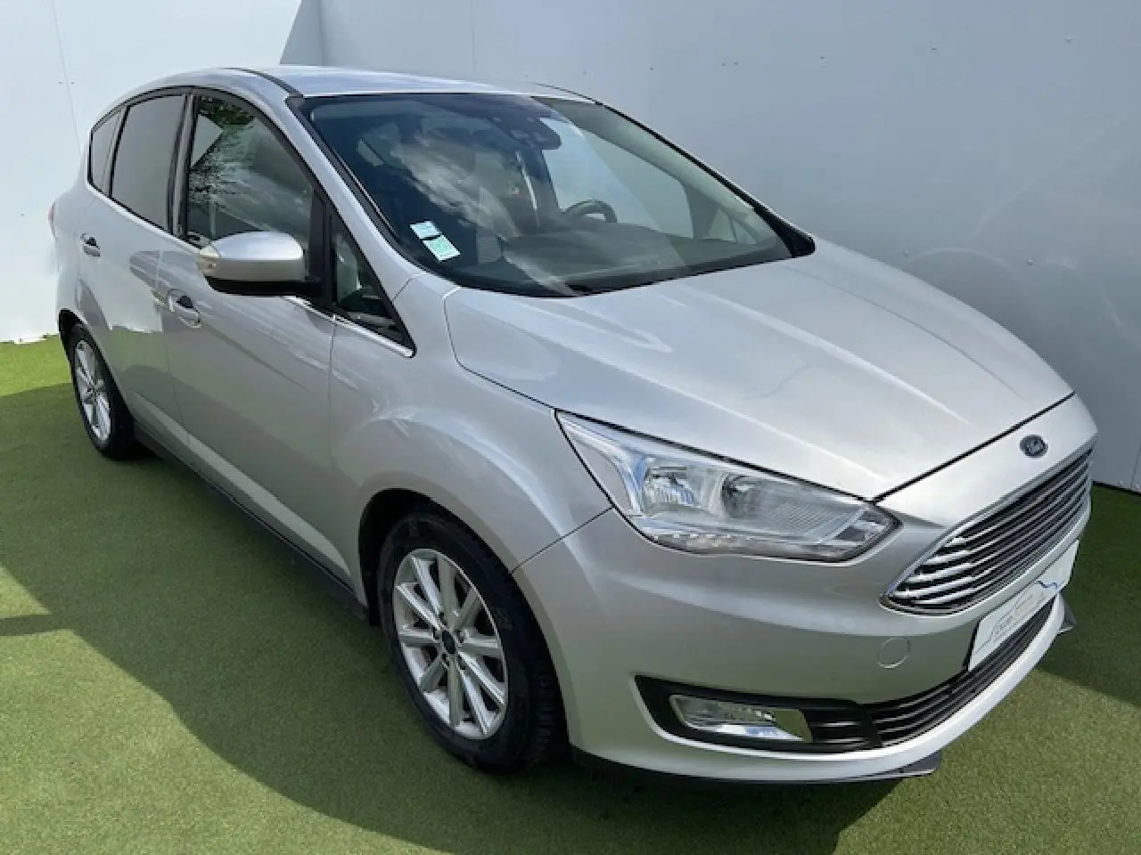 Ford C-MAX II gris clair métal vu en 3/4 avant droit, avec calandre chromée et jantes alliage 16 pouces.