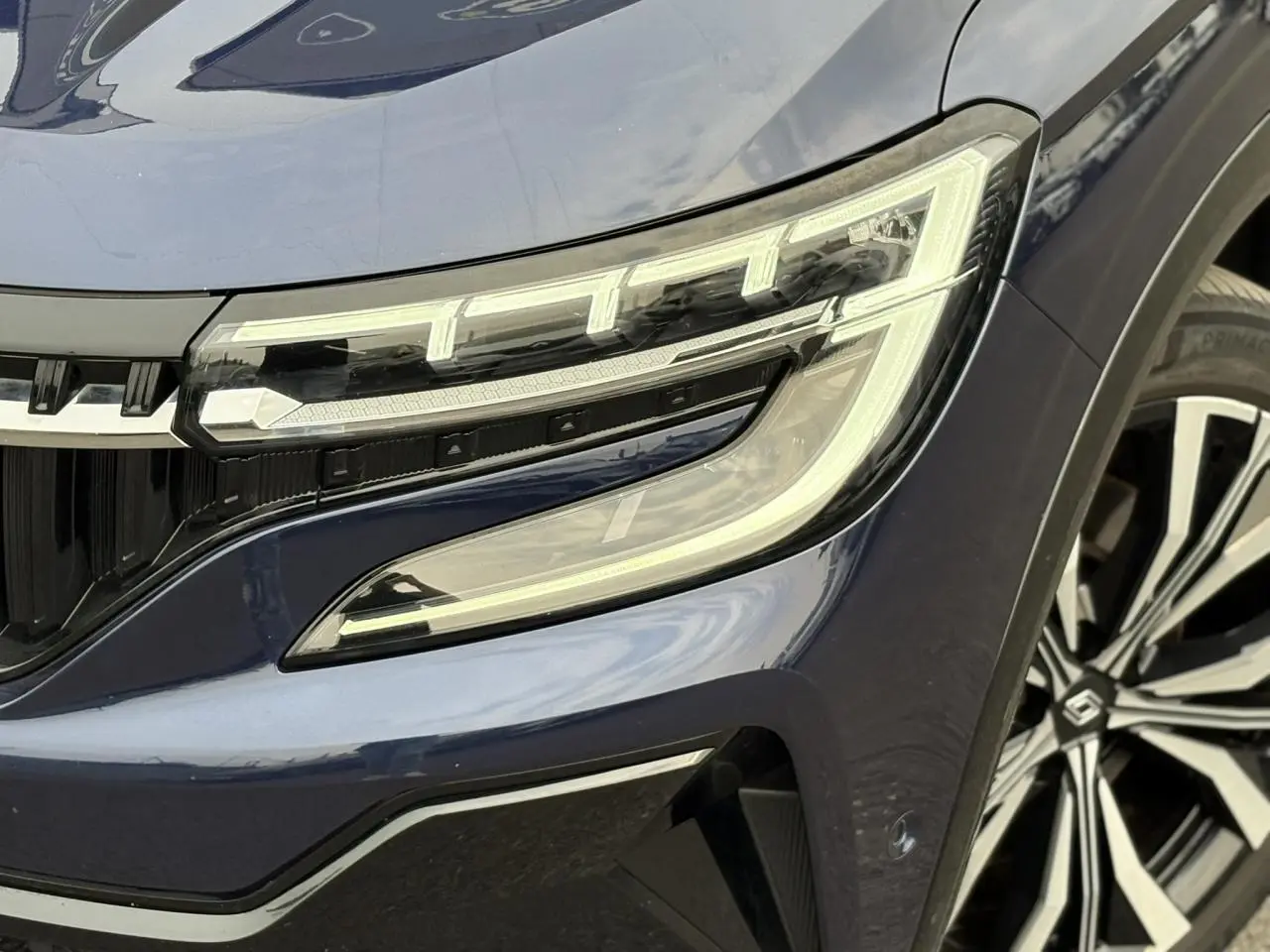 Gros plan sur le phare avant droit et la jante diamantée noire du Renault Espace Bleu Nuit 2023.