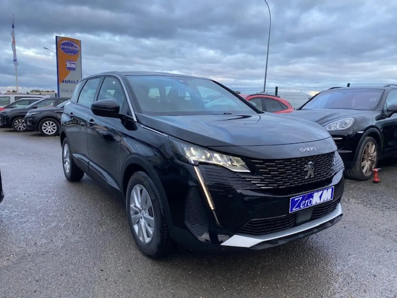 Peugeot 5008 noir vue 3/4 avant gauche sur parking, avec calandre distinctive et feux LED allumés.