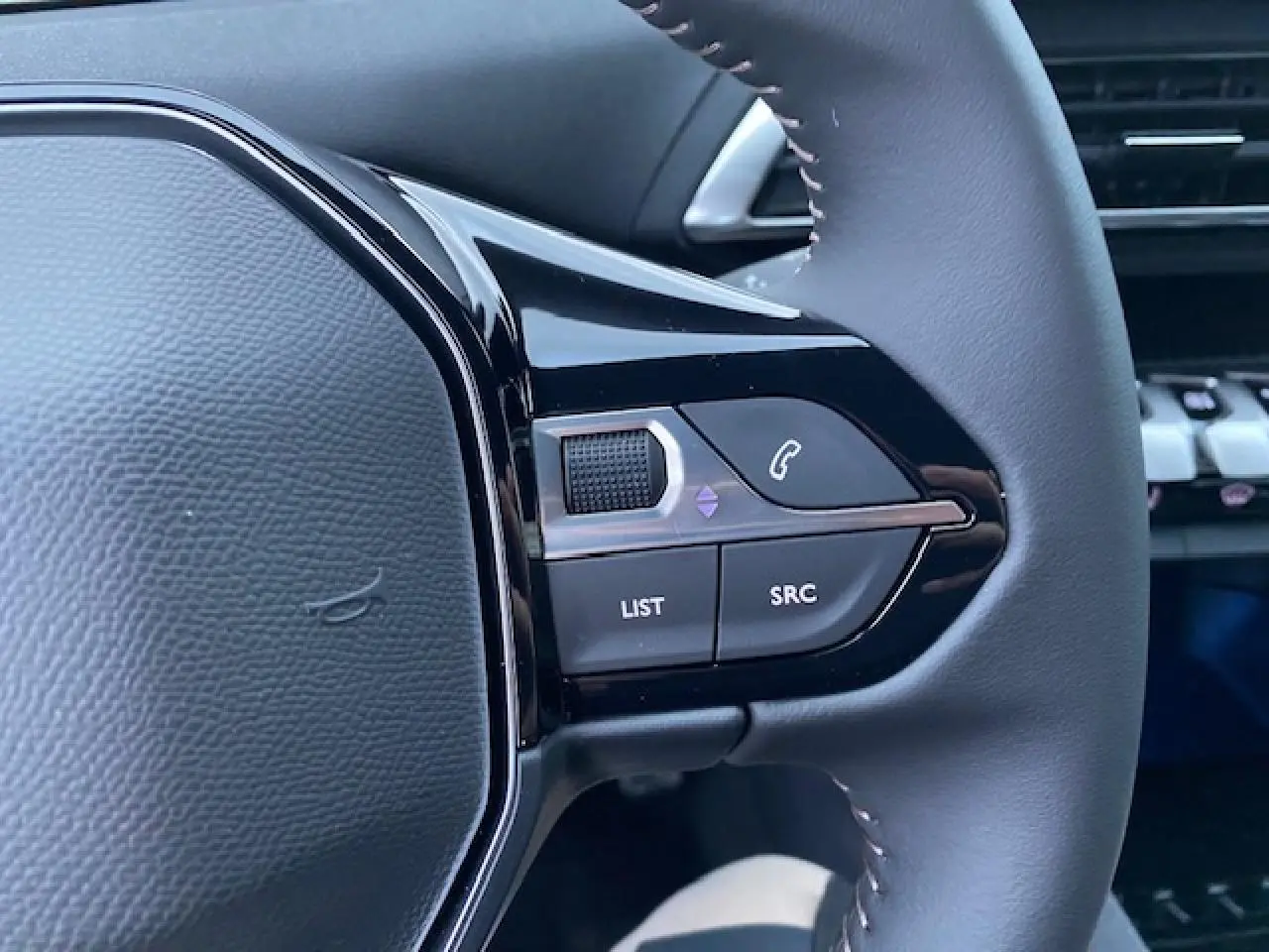 Gros plan sur les commandes du volant côté gauche du Peugeot 5008 noir, avec boutons de téléphone et menu.
