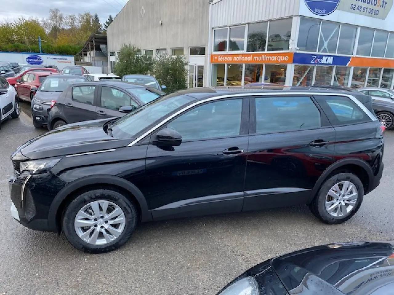 Peugeot 5008 noir vue de profil côté gauche, avec jantes alliage et carrosserie brillante sous un ciel nuageux.