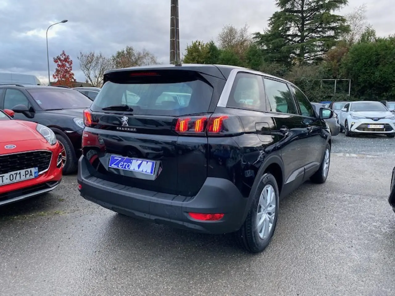 Peugeot 5008 noir vue 3/4 arrière droit, feux arrière LED allumés, jantes alliage 16 pouces, stationnée en extérieur.