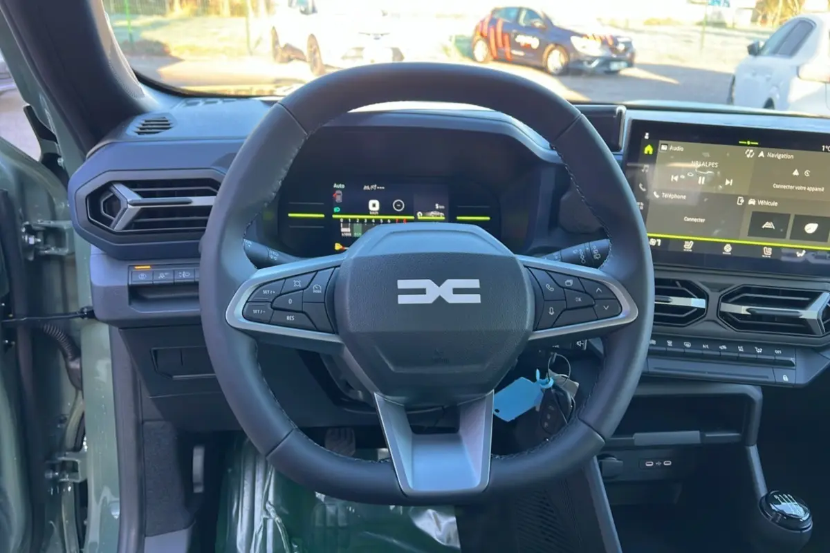 Vue intérieure centrée sur le volant du Dacia Duster 2025 kaki lichen, avec tableau de bord numérique et écran tactile.