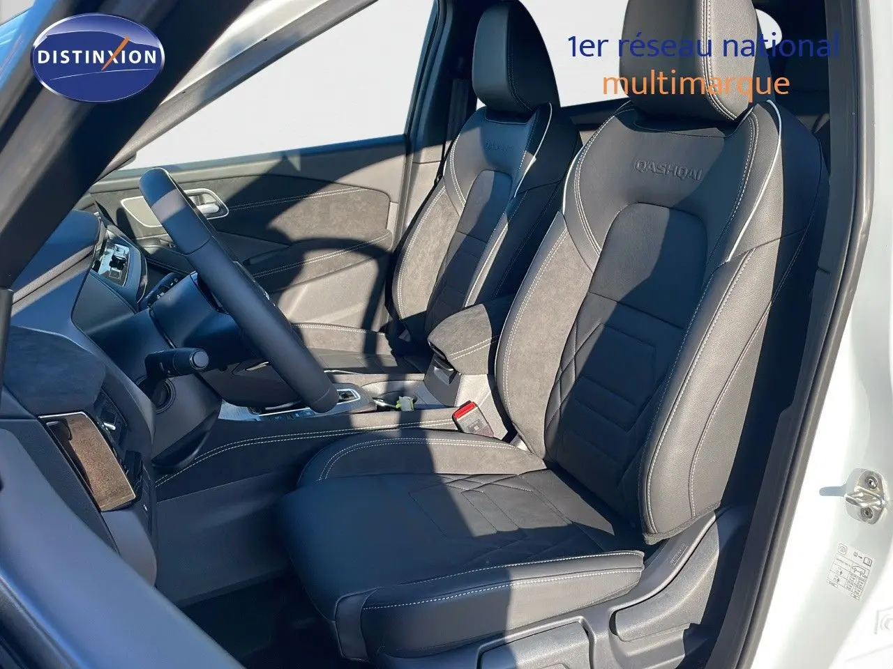 Intérieur du Nissan Qashqai 2025 en blanc nacré, vue côté gauche sur sièges en cuir noir avec logo Qashqai brodé.