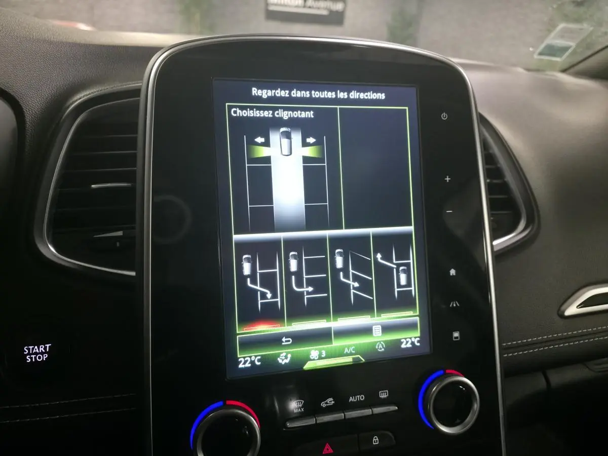 Écran tactile central du tableau de bord du Renault Scénic noir, affichant l'aide au stationnement avec choix de clignotant.