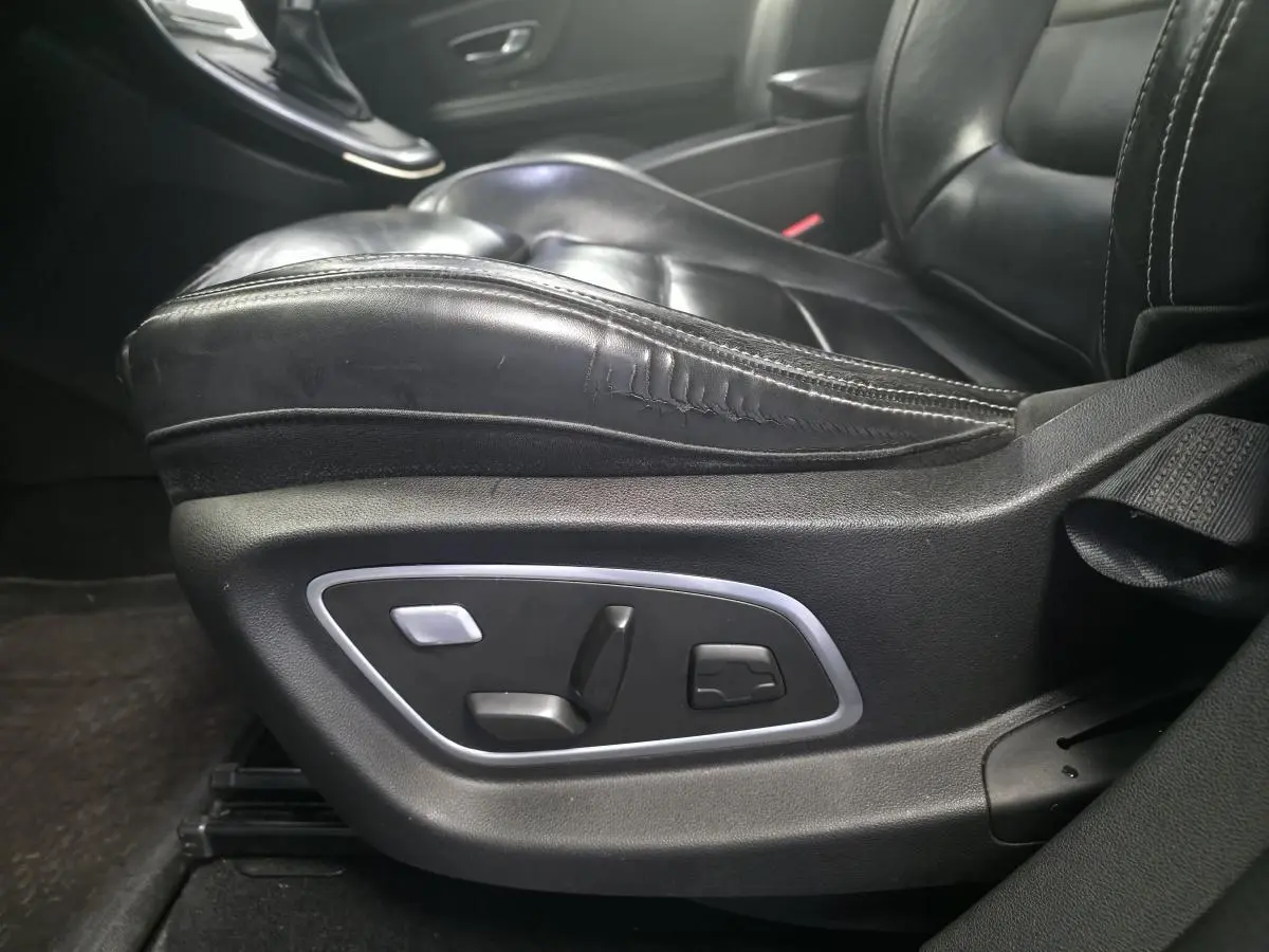 Gros plan sur le siège conducteur en cuir noir avec commandes électriques sur le côté d'un Renault Scenic IV Initiale Paris.