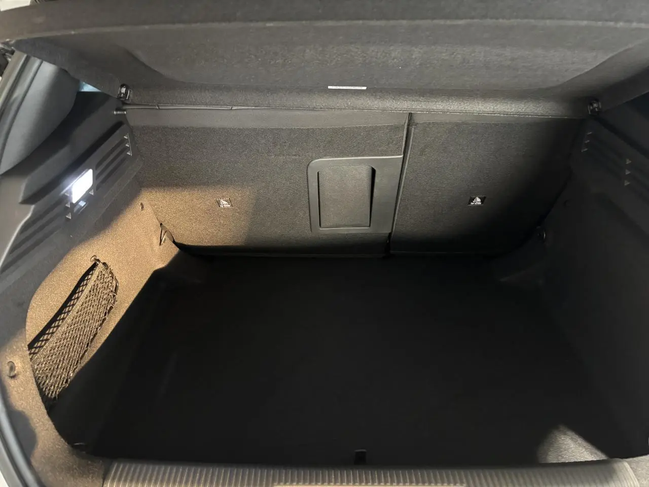 Coffre ouvert de la Peugeot 308 hybride blanche, vue intérieure montrant un espace de rangement propre et bien éclairé.