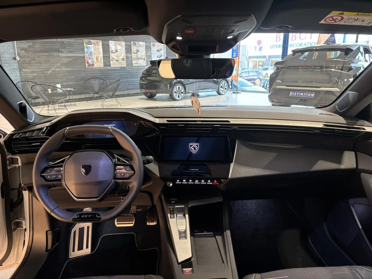 Vue intérieure frontale du poste de conduite de la Peugeot 308 Hybrid blanche avec volant GT et écran tactile central.