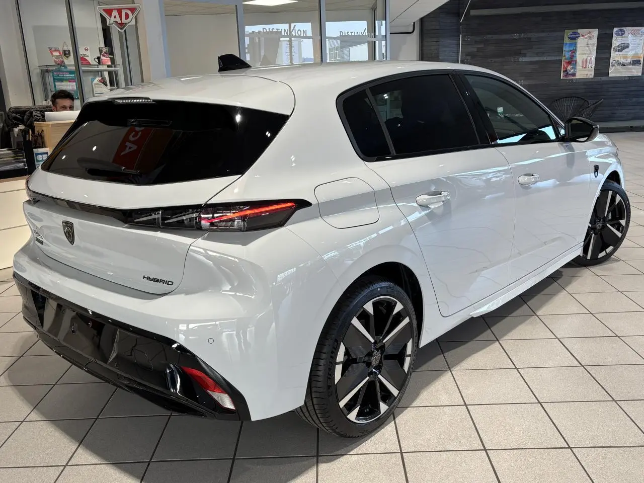 Vue 3/4 arrière droite d'une Peugeot 308 hybride blanche Okenite avec jantes alliage bicolores et vitres teintées.