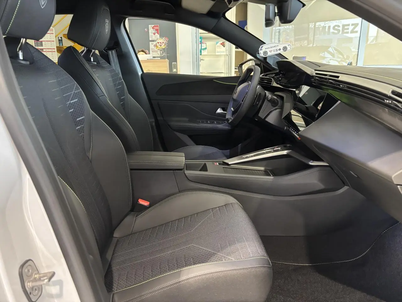 Vue intérieure côté conducteur du Peugeot 308 blanc Okenite 2026, avec sièges noirs et surpiqûres vert Adamite.