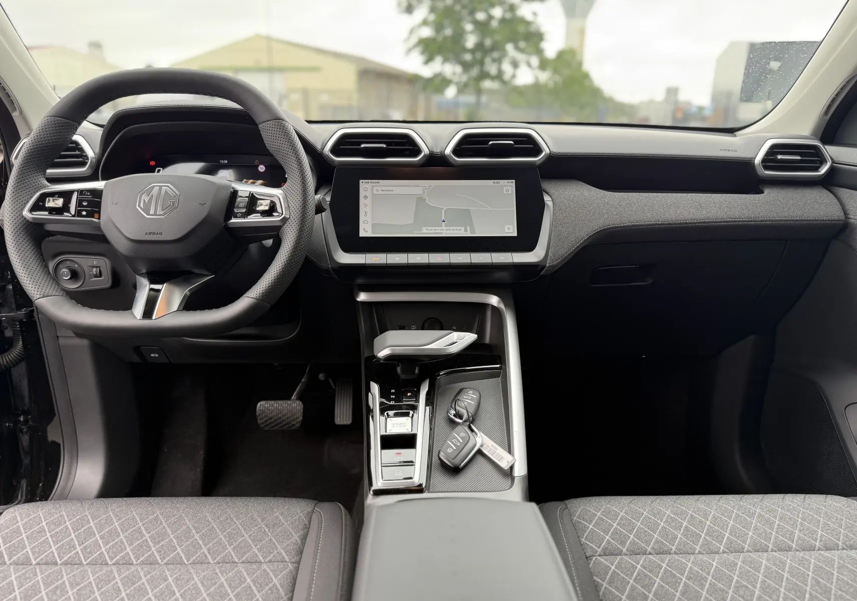 Vue intérieure frontale du tableau de bord et volant noir du MG ZS 1.5L Hybrid+ avec écran tactile et clés sur la console centrale.