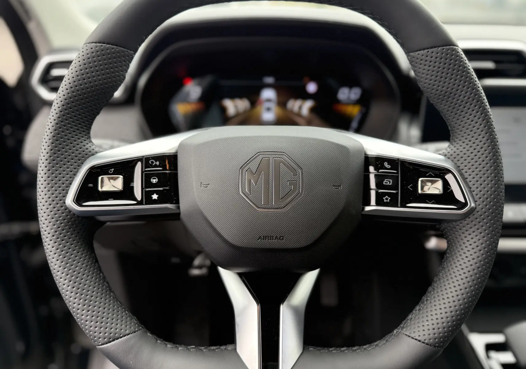 Vue rapprochée du volant perforé noir avec logo MG au centre du MG ZS 1.5L Hybrid+ 2026, boutons multifonctions visibles.