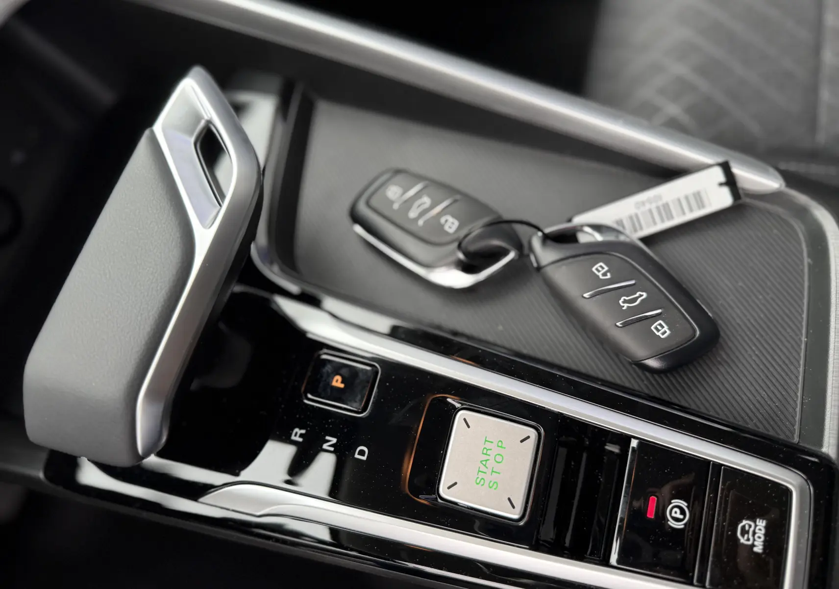 Gros plan sur la console centrale du MG ZS 1.5L Hybrid+ 2026 avec levier de vitesse, bouton start/stop et clés posées.