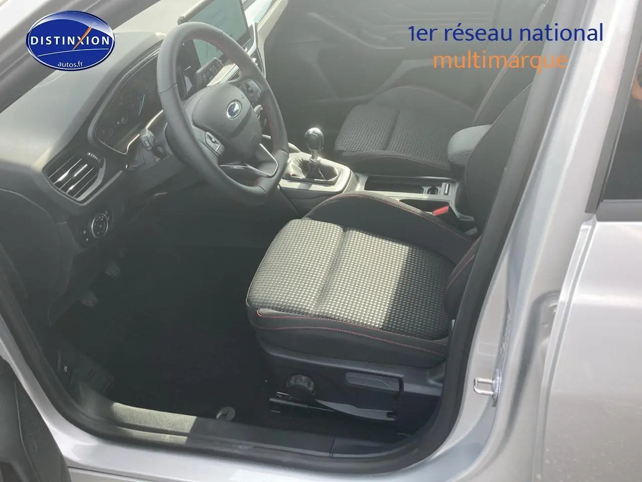 Intérieur avant droit de la Ford Focus gris 2025, volant trois branches avec coutures rouges et boîte manuelle visible.