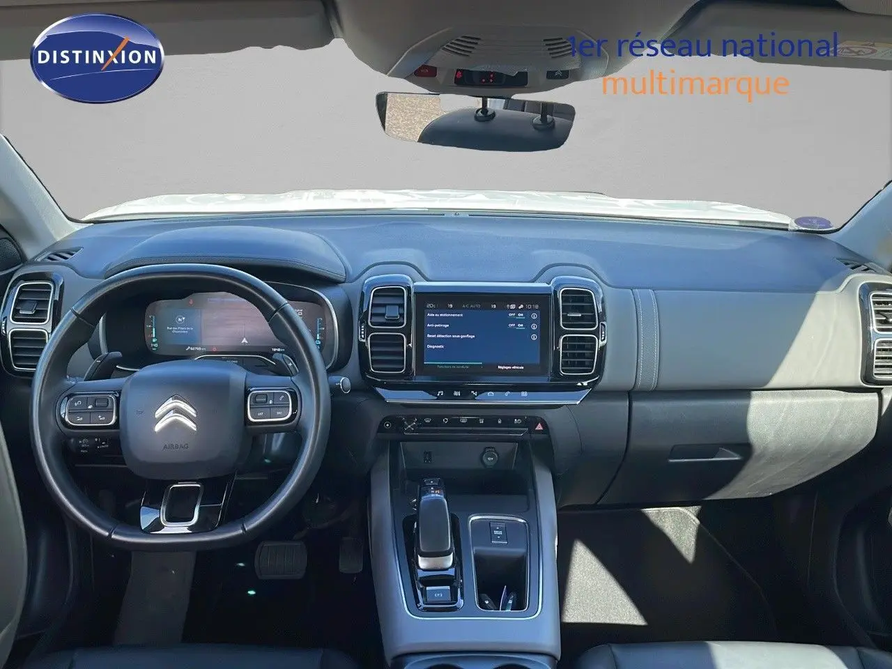 Vue intérieure du tableau de bord et volant noir du Citroën C5 Aircross blanc nacré hybride, avec écran tactile central allumé.