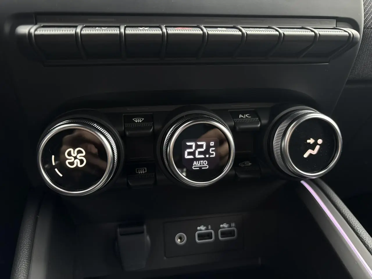 Gros plan sur les commandes de climatisation digitale et les ports USB dans l'habitacle noir de la Renault Clio 2025.